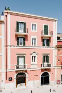马泰拉Palazzo della Fontana的粉红色的建筑,设有绿色窗户和阳台
