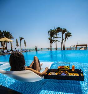 艾因苏赫纳Cancun Sokhna Resort & Villas的坐在椅子上的女人,在游泳池里拿着一盘食物