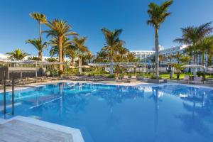 马斯帕洛马斯Hotel Riu Palace Maspalomas - Adults Only的一座棕榈树的大型游泳池,以及一间位于酒店后面的酒店