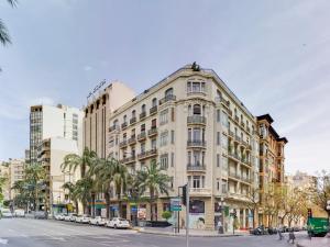 阿利坎特阿方索十世公寓的一座大型白色建筑,位于一条种有棕榈树的城市街道上
