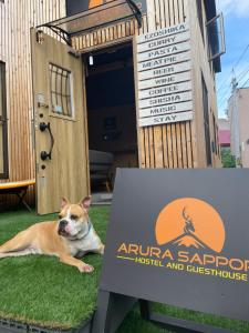 札幌Arura Sapporo的一只狗躺在标牌前的草地上