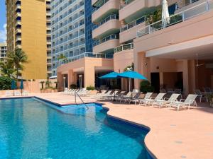 阿卡普尔科Comfortable Beachfront apartment in Acapulco的一座带椅子和遮阳伞的游泳池位于一座建筑旁边