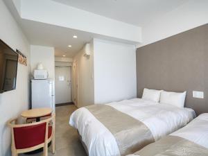 那霸BiBi Hotel NAHA KUME的一间卧室配有两张床、一张桌子和一台冰箱