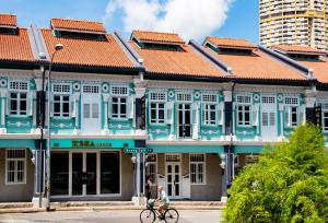 新加坡KēSa House, The Unlimited Collection managed by The Ascott Limited的一位在蓝色建筑前骑着自行车的女人
