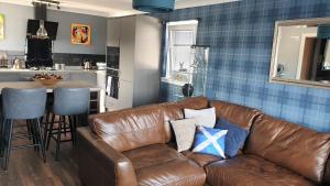 巴洛赫Holiday Apartment, Balloch, Loch Lomond的一间带棕色真皮沙发的客厅和一间厨房