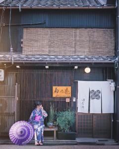 名古屋一棟貸切宿Machiya Kikunoya Hanare的坐在一座紫色伞的建筑前的女人