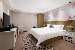 广州Paco Hotel Gangding Metro Guangzhou的酒店客房设有一张白色大床和电视。
