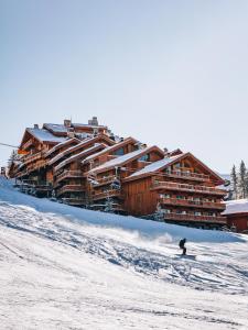 美贝尔Hotel Le Coucou Méribel的滑雪者在小屋前的雪覆盖的斜坡上滑雪