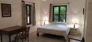 蓬蒂切里Isai Ambalam guest house的一间卧室配有一张床、一张桌子和两个窗户