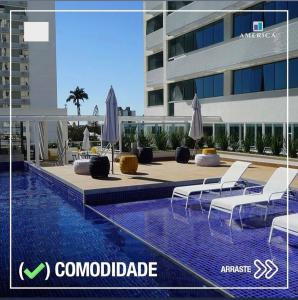 坎普斯戈伊塔卡济斯Flat Apart Hotel América Campos dos Goytacazes的一座带椅子和遮阳伞的游泳池位于一座建筑旁边