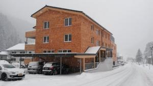 克勒施特勒Alpine Lodge Klösterle am Arlberg的积雪中一座大型砖砌建筑,有停放的汽车