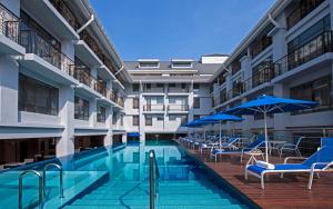 乔治市槟城皇家朱兰酒店的一座大楼内的游泳池,配有椅子和遮阳伞