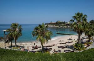 库萨达斯松树湾旅游度假酒店的棕榈树和遮阳伞的海滩,以及海滩上的人