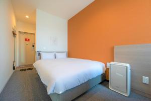 InadaHOTEL R9 The Yard Hitachinaka的橙色墙壁的房间里一张大白色的床