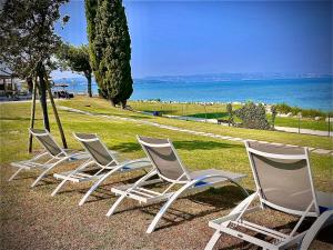 代森扎诺-德尔加达Hotel Aquila D'Oro Desenzano的坐在水边的草地上,四把白色椅子