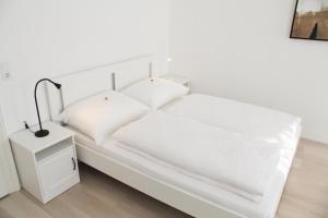 维也纳Vienna4you App 33 you are welcome的白色的床,带白色床单,床头柜上配有一盏灯