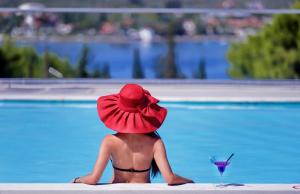 PuntaHotel Punta的坐在游泳池旁的红帽上的女人