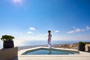 皮尔戈斯Santorini Sky, The Lodge的站在游泳池边俯瞰大海的女人