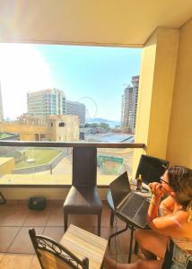 迪拜DXB Backpackers的坐在桌子上的女人,在窗前用笔记本电脑