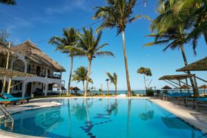 MakunduchiNest Style Beach Hotel Zanzibar的棕榈树和海洋的度假村游泳池