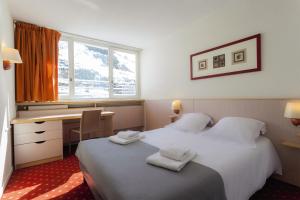 里蒙纽耶Belambra Clubs Les Menuires - Neige Et Ciel的酒店客房设有两张床、一张书桌和一个窗户。