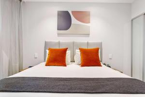 奥克兰Ramada by Wyndham Newmarket Auckland的卧室配有带橙色枕头的白色床