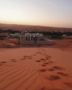 Al RakaPrivate Sand Bond的沙漠中的一座有沙地脚印的建筑