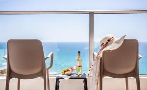 内坦亚Ramada Hotel & Suites by Wyndham Netanya的坐在椅子上的女人,带一瓶葡萄酒