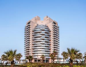 内坦亚Ramada Hotel & Suites by Wyndham Netanya的一座高大的建筑,前面有棕榈树