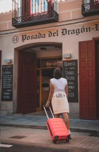 马德里波萨达德尔龙精品酒店的一位女士在大楼前拉着一个红色的手提箱