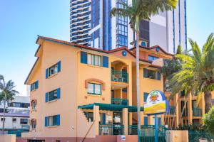 黄金海岸阿鲁巴金沙度假酒店的一座黄色的建筑,有棕榈树和高大的建筑
