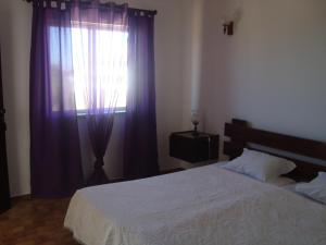 萨格里什米拉福塔雷萨宾馆的一间卧室配有一张床和一个带紫色窗帘的窗户
