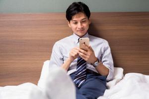 成田成田机场康福特茵酒店的坐在床上看手机的人