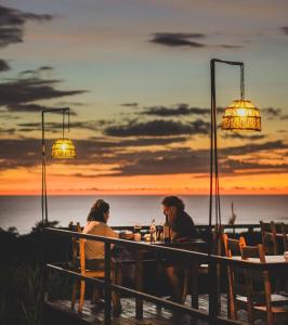 圣塔特蕾莎海滩Hotel Buenos Aires的两人坐在桌子旁,背着日落