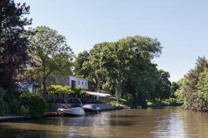根特Hotel Nenuphar的一条河,船停靠在房屋和树木旁边