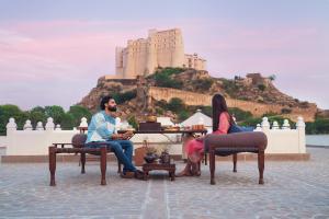 斋浦尔Alila Fort Bishangarh Jaipur - A Hyatt Brand的两人坐在桌子上,背靠城堡