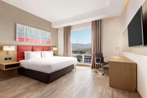 马斯喀特Ramada Encore by Wyndham Muscat Al-Ghubra的酒店客房设有一张床和一个大窗户