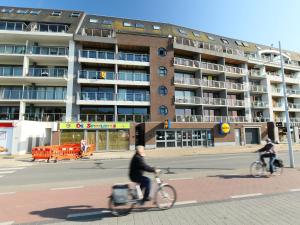 布列登Apartment Residentie Albatros by Interhome的两个人骑着自行车沿着大楼前的街道骑着