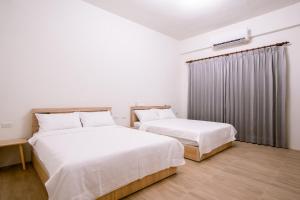 Huxi澎湖逸軒居民宿的配有白色墙壁和木地板的客房内的两张床