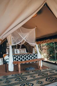 塔勒克Emboo River Camp的帐篷内的天蓬床和长凳