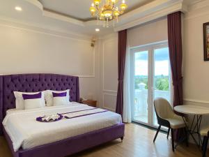 大叻Peach Valley Hotel Dalat的一间卧室配有紫色的床、桌子和窗户。