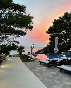 乌尔齐尼Pino Boutique Hotel的一个带长椅和遮阳伞的游泳池,并可欣赏日落美景