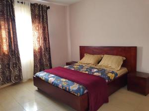 雅温得Appartement chic au quartier Omnisport的一间卧室配有一张带木制床头板和窗帘的床。