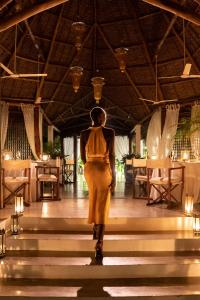 马林迪Lion in the Sun Billionaire Retreat Malindi的穿着黄色衣服的女人走在餐馆的楼梯上