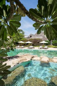 马林迪Lion in the Sun Billionaire Retreat Malindi的游泳池拥有蓝色的水、岩石和遮阳伞