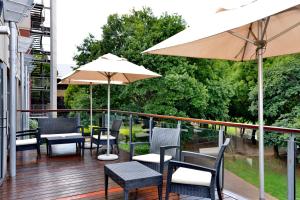 鲁德普特ANEW Hotel Roodepoort Johannesburg的阳台配有桌椅和雨伞。
