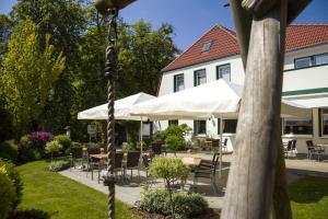 诺尔德霍尔茨Landgasthof "Zum grünen Walde"的一个带桌椅和白色遮阳伞的庭院。