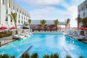 马斯喀特Maani Muscat Hotel & Suites的一座带椅子和遮阳伞的游泳池位于一座建筑旁边