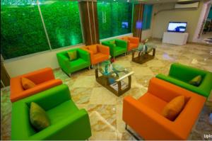 达卡Hotel Gulshan Lake View的客厅配有橙色和绿色椅子以及电视
