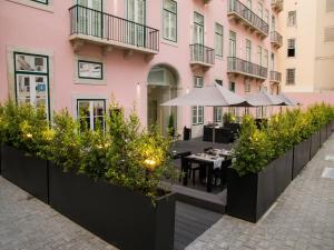 里斯本葡萄牙精品酒店的一座粉红色建筑前方的户外庭院,配有桌子和植物